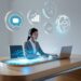 A headset-wearing rep types on a slim laptop while floating chat, analytics, and 24_7 clock icons orbit; concept of AI in customer-service